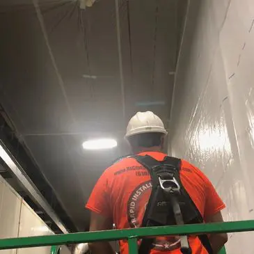 A man in an orange shirt and helmet on a green ladder.