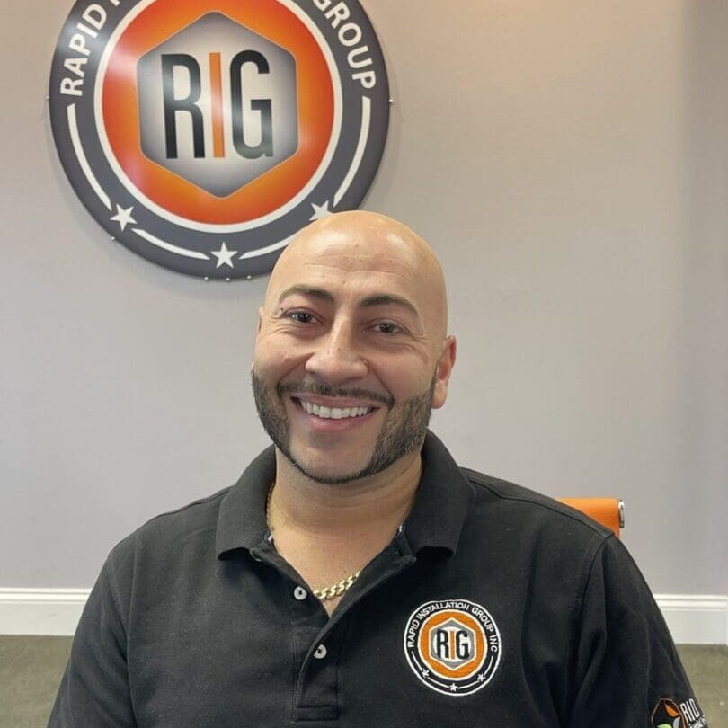 A man in black shirt sitting on chair next to rig logo.